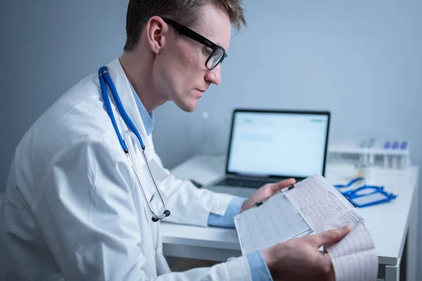 Cardiologist reading an ECG print-out. Doctor analyzing electrocardiogram. Practitioner examine patient test results. Medical and healthcare concept. Physician looking at cardiogram at medical office.