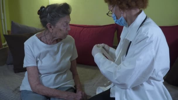 Una mujer mayor está siendo examinada para el coronavirus en casa. Un médico con bata de laboratorio toma hisopo de covid 19 de la mujer mayor de la garganta en el asilo de ancianos. Prueba rápida del antígeno durante la pandemia del coronavirus — Vídeo de stock