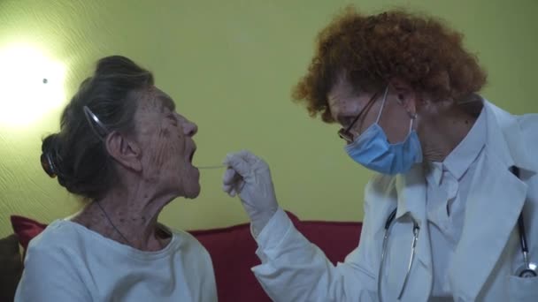 Female doctor visits senior woman at nursing home and takes throat swab coronavirus infection. Old patient passing medical test on covid 19 at home for the elderly. Doing COVID test to senior woman — Vídeo de Stock