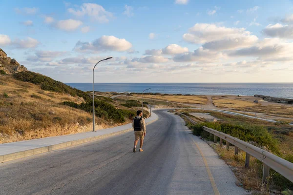 Male tourist hikers on an asphalt mountain road overlooking the sea in Cyprus near Agios Georgios Pegeias. Roadway leading to bay on mediterranean sea. Travel and freedom, adventures and travel — ストック写真