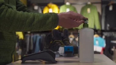 Salesman disinfecting hands sanitizer alcohol gel behind counter of sports store close-up. Seller washing both hands before starting work. Concept new rules for business during pandemic. New normal
