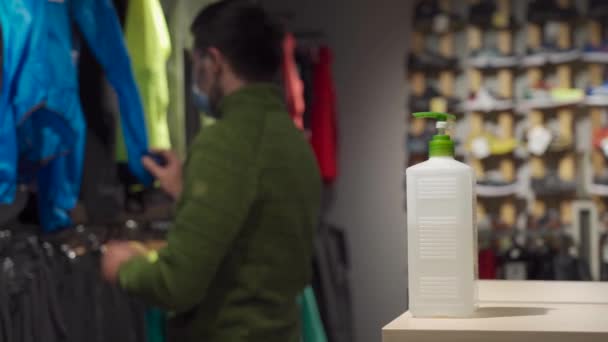 Topic of buying sportswear in offline sports store during new norms pandemic for covid 19. Man wearing mask chooses jacket in an outdoor store. Masked male looking to buy jacket during shopping — Stock video