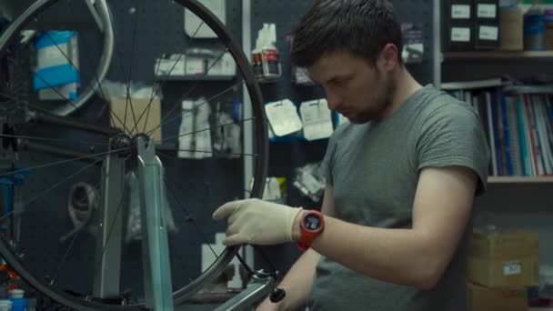 Bicycle repair and maintenance. Wheel rim alignment tool. Man in gloves aligns spokes of bicycle. Bike repairman with specialized tool in workshop tightening wheel spokes. Cycle mechanic fixes wheel — Stock Video