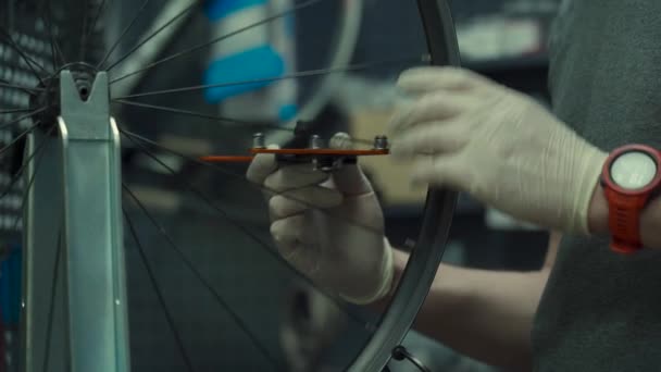 Wheel straightening stand in bicycle workshop. Mechanic uses tool to tension the spokes in rim of velocipede wheel. Small business bike repair and service theme. Truing cycle wheel. Repairman — Wideo stockowe