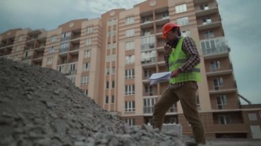 Inspecting builder speaks angrily on phone with subordinate at construction site checks amount of crushed stone for the construction of road in residential area according to incoming invoices