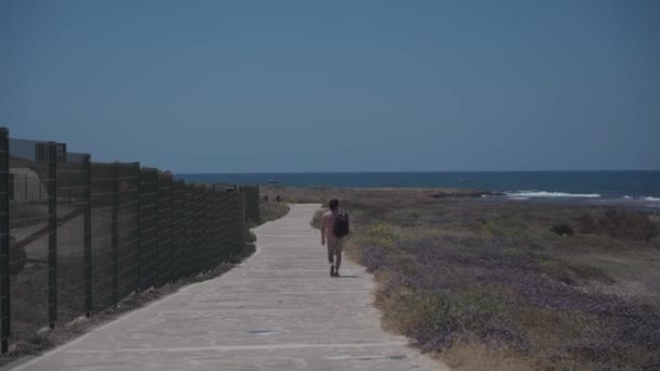Человек турист с рюкзаком прогулка вдоль пешеходной дорожки на скалистом побережье Средиземного моря в городе Пафос Кипра в летнюю солнечную погоду. Прибрежный Бродвей. Исследуйте остров Кипр пешком. Пешие прогулки — стоковое видео