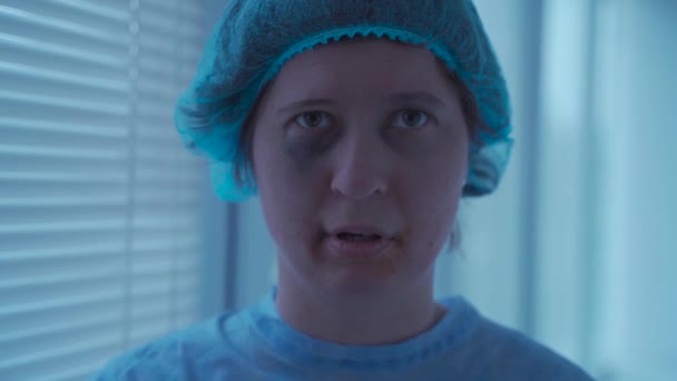 Crazy stressed woman with face and dental injuries in medical uniform in a hospital is scared and interested in looking somewhere. Mental disease patient. Suffering from mental disorder — Vídeo de Stock