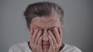 Yaşlılara karşı aile içi şiddet. Son sınıf öğrencisi kadın korkmuş ve ağlıyor, elleriyle gözlerini ovuyor ve gri arka plandaki kameraya bakıyor. Olgun bir kadın, elleri yüzünde ağlıyor. Yalnızlık