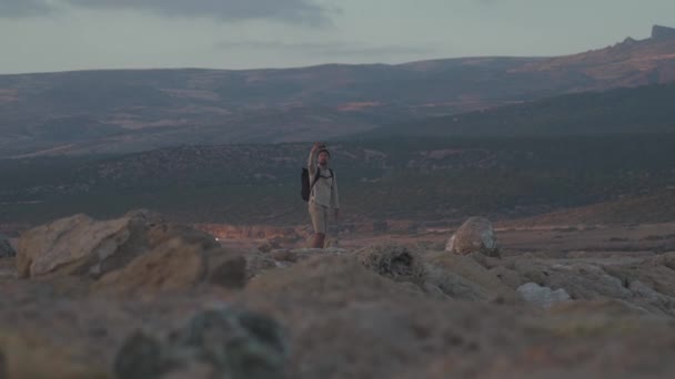 El viajero mantiene el blog de viajes tomando fotos y videos con teléfono inteligente mientras camina a lo largo del mar rocoso de la costa en la isla de Cyprus al atardecer. Mochilero haciendo foto de paisaje marino en la costa rocosa en el teléfono — Vídeos de Stock