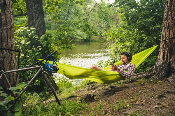Человек Велосипеде Кемпинге Озера Отдыхает Зеленом Гамаке Слушая Музыку Активная — стоковое фото