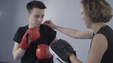 Kolları boks pençeli bir kadın acemi kadın dövüşçüye sakso tekniği öğretiyor. Boks, MMA, Muay Thai antrenörleri ve sporcularla temas kuran partnerler. Tekvandonun kişisel dövüş sanatı