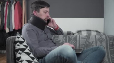 Evden çalışan boyunluk takan serbest çalışan bir adam. Dizüstü bilgisayarda çalışan bir erkek, telefonda koltukta konuşuyor. Boyun ağrısından muzdarip. Omurilik zedelenmesi olan adam arıyor.
