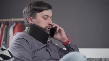 Evden çalışan boyunluk takan serbest çalışan bir adam. Dizüstü bilgisayarda çalışan bir erkek, telefonda koltukta konuşuyor. Boyun ağrısından muzdarip. Omurilik zedelenmesi olan adam arıyor.