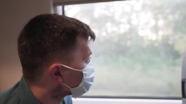 Mannen med skyddande ansiktsmask tittar sorgset ut genom tågfönstret. Förebyggande åtgärder. Nytt normalt pandemikoncept. Resa säkert på järnväg kollektivtrafik. Avbryt COVID-19-infektion — Stockvideo