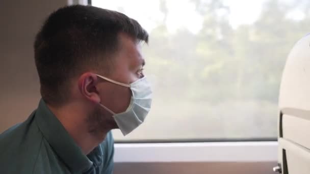 Zmęczony smutny pasażer z medyczną maską ochronną przed infekcją koronawirusową, covid-19 siedzi w pociągu i patrzy przez okno. Nowa normalność. Odległość społeczna podczas podróży środkami transportu publicznego — Wideo stockowe