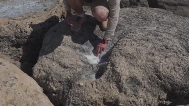 Mannelijke geoloog onderzoekt monsters van kristallen zeezout uit de rotsen in de buurt van zee. Mariene geoloog onderzoekt mineraal monster verdampt uit de zee op een rotsachtig gebied. Geologie onderzoeker op zoek naar monsters — Stockvideo