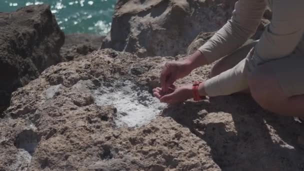 O tema é geologia e pesquisa de cristais e rochas de origem natural. Um explorador macho recolhe amostras de sal marinho numa rocha perto do Mar Mediterrâneo, na ilha de Chipre. Geólogo no trabalho — Vídeo de Stock