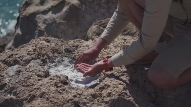 Ämnet är geologi och forskning av kristaller och stenar av naturligt ursprung. En manlig upptäcktsresande tar prover av havssalt på en klippa nära Medelhavet på ön Cypern. Geolog på jobbet — Stockvideo