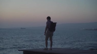 Sırt çantalı gezgin gün batımını ve Akdeniz manzarasını Cythe Adası 'ndaki ahşap iskeleden seyrediyor. Özgürlük kavramı. Seyahat, günbatımının tadını çıkaran erkek, yalnız gezgin.