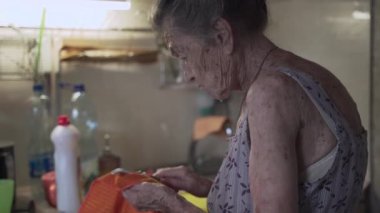 Mutfakta bulaşık yıkayan yaşlı bir kadın. Üzgün olgun ev hanımı mutfaktaki eski bulaşıkları yıkar. Gri saçlı üzgün bir kadın. 90 yaşında. Mutfak aletlerini evde yıkıyor.