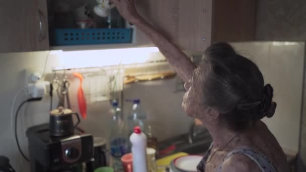 Oudere vrouw die afwas in de keuken. Droevige volwassen huisvrouw ruimt de oude borden in de keuken op. Verontrustende vrouw met grijs haar 90 jaar oud was keukengerei in een handwas thuis — Stockvideo