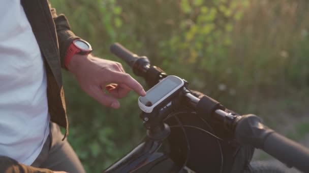 Велосипедист пользуется велосипедным компьютером на руле горного велосипеда в природе. Путешественник на велосипеде смотрит на карту, строит маршрут с помощью GPS на велосипеде навигатора. Деятельность трекер и оффлайн карты для езды на велосипеде — стоковое видео