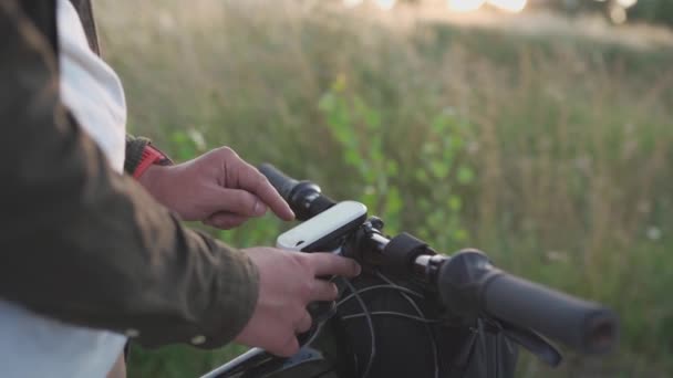 Άνθρωποι, αθλήματα, ενεργός τρόπος ζωής. Ποδηλάτης χρησιμοποιώντας συσκευή πλοήγησης εξετάζει χάρτη και ψάχνει για συντεταγμένες GPS στην οθόνη του gadget, ενώ ποδηλασία σε εξωτερικούς χώρους. Ανιχνευτής δραστηριότητας στο τιμόνι του κύκλου — Αρχείο Βίντεο