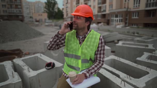 Erkek ustabaşı, işçi ya da mimar inşaat alanında çalışıyor çay ya da kahve içiyor ve cep telefonuyla konuşuyor. Gerisi üretim paketinin bir parçası. — Stok video