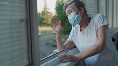90 'ların sonlarında maskeli yaşlı bir kadının portresi ev penceresinden el sallıyor. Koruyucu maskeli yaşlı kadın pencereden dışarı bakar ve evde yalnızken elini sallar ve sosyal mesafeyi yönetir..