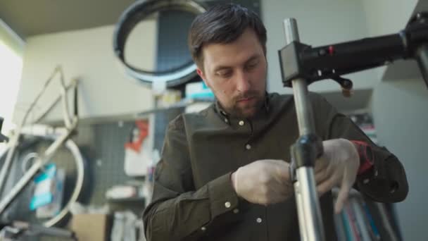 Technical expertise taking care bicycle shop. Attractive mechanic is fixing customers bicycle at his own workshop. Technician fixes bicycle suspension fork in workroom. Bicycle shop, bicycle service — Stock Video