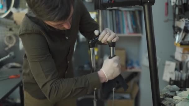 Ekspertyza techniczna zajmująca się sklepem rowerowym. Atrakcyjny mechanik naprawia rowery w swoim warsztacie. Technik naprawia widelec rowerowy w pracowni. Sklep rowerowy, serwis rowerowy — Wideo stockowe