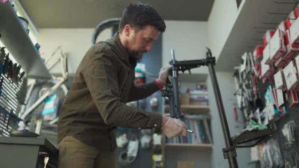 Experiência técnica tendo loja de bicicletas cuidado. Mecânico atraente é a fixação de clientes de bicicleta em sua própria oficina. Técnico corrige garfo de suspensão de bicicleta na sala de trabalho. Loja de bicicletas, serviço de bicicletas — Vídeo de Stock