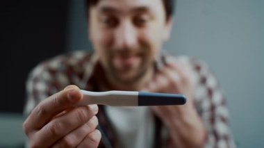 Evde hamilelik testi yapan mutlu ve neşeli bir beyaz adam. Genç gelecekteki babalığın mutluluk teması. Müstakbel baba olmak ne büyük mutluluk. Mutlu erkek hamilelik testi sonuçlarını kontrol ediyor.