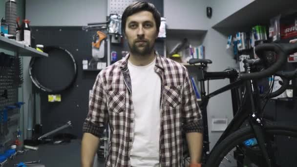 Mécanicien de vélo dans l'atelier de service de vélo posant sur le lieu de travail, montrant la force dans les mains en levant les outils au-dessus de la tête. Technicien cycliste portrait montrant joyeusement les muscles avec outil dans le magasin de vélo — Video