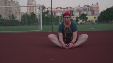 Stadyumda antrenmandan sonra esneme hareketleri yapan beyaz bir kadın. Kilolu bir kadın açık hava spor sahasında geriniyor. Sportif insanlar yaşam tarzı konsepti. Sakin ol ve spor yap.