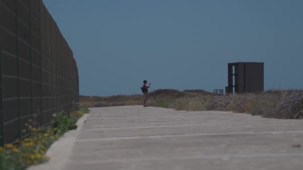 Muž turista s batohem procházka podél pěší stezky na skalnatém pobřeží Středozemního moře ve městě Paphos Kypru v létě slunné horké počasí. Pobřežní Broadwalk. Prozkoumejte ostrov Kypr pěšky. Turistika — Stock video