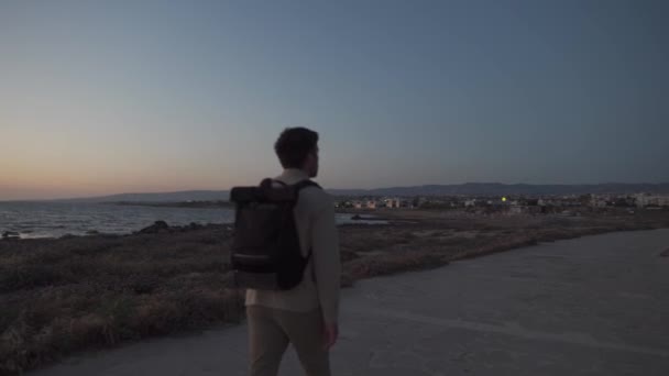 Muž turista s batohem procházka podél pěší stezky na skalnatém pobřeží Středozemního moře ve městě Paphos Kypru v létě slunné horké počasí. Pobřežní Broadwalk. Prozkoumejte ostrov Kypr pěšky. Turistika — Stock video