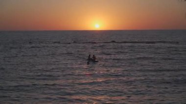 İki kız Güney Amerika 'nın paphos şehrinde gün batımında sakin Akdeniz' de yemek masasında oturur. Gün batımında kürek çeken iki kızın siluetleri. Gün batımında sahile yakın su sporu