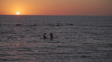 Akdeniz 'de, günbatımında Akdeniz' de sakin sularda kürek çeken iki kadın. SUP 'de kürek çeken iki kız. Silhuette uzakta. Su sporu, yemek sörfü, sörf tahtası ya da kürek sporcusu.