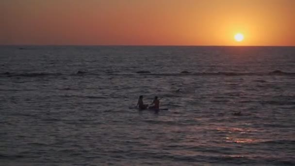 Deux femmes partageant la planche à pagaie au coucher du soleil sur des eaux calmes dans la mer Méditerranée à Cyprus. Deux filles en train de pagayer sur SUP. Silhuette au loin. Sports nautiques, surf sup, planche de surf ou planche à pagaie — Video