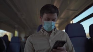 Yeni normalin konusu ve koronavirüs salgını sırasında seyahat etmek: koruyucu maskeli bir adam trende seyahat eder ve akıllı telefon kullanır. İyi yolculuklar. Toplu taşımacılıkta sosyal uzaklık