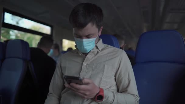 Людина в масці зі смартфоном, що подорожує потягом. Кавказький чоловік носить антивірусні маски на громадському транспорті. У масках пасажири користуються смартфоном під час подорожі залізницею на приміському поїзді. — стокове відео