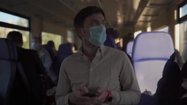 Yeni normalin konusu ve koronavirüs salgını sırasında seyahat etmek: koruyucu maskeli bir adam trende seyahat eder ve akıllı telefon kullanır. İyi yolculuklar. Toplu taşımacılıkta sosyal uzaklık