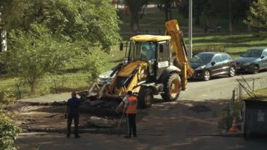 Ukrayna, Kiev, 15 Eylül 2021. İşçiler asfaltı kazıcının kovasına koyarak çıkarıyorlar. Yol çalışmaları sırasında asfalt yolda bir grup işçiyle buldozer. Yol yapımı