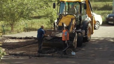 Ukrayna, Kiev, 15 Eylül 2021. Pençeli işçiler asfaltı yoldan çıkarıp kazı kovasına koyuyorlar. Yol onarımı ağır iş. Kürek işçileri eski asfaltın yerini aldı