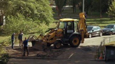 Ukrayna, Kiev, 15 Eylül 2021. İşçiler asfaltı kazıcının kovasına koyarak çıkarıyorlar. Yol çalışmaları sırasında asfalt yolda bir grup işçiyle buldozer. Yol yapımı