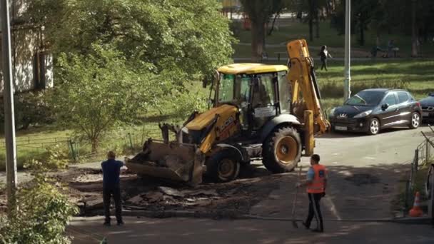 乌克兰基辅，2021年9月15日。工人们用爪子把沥青路面从路上取出，堆放在挖掘机的桶里。修路方便,重活要做.Shovel workers replace old asphalt — 图库视频影像