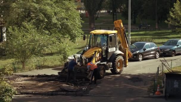 Ucrania, Kiev, 15 de septiembre de 2021. Equipo de trabajadores de reparación de carreteras elimina el asfalto viejo con palas y equipo de construcción en cucharón excavadora mientras se construyen carreteras en el patio del edificio de apartamentos — Vídeo de stock