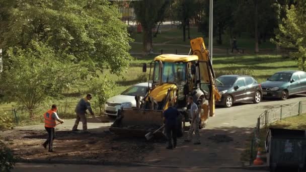 Ukraine, Kiew, 15. September 2021. Team von Straßenreparaturarbeitern entfernt alten Asphalt mit Schaufeln und Baumaschinen in Baggerlöffel beim Straßenbau im Hof eines Mehrfamilienhauses — Stockvideo