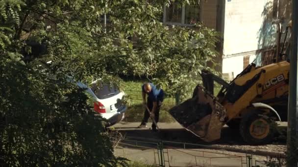 Ukrajina, Kyjev, 15. září2021. Tým silničních opravářů odstraňuje starý asfalt s lopatami a stavebním zařízením do sběračské sběračky při stavbě silnic ve dvoře činžovního domu — Stock video